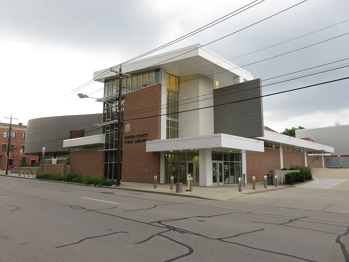 Modern two-story library building of brick, glass and white panels on a street corner, with a "Kenton County Public Library" sign by the entrance